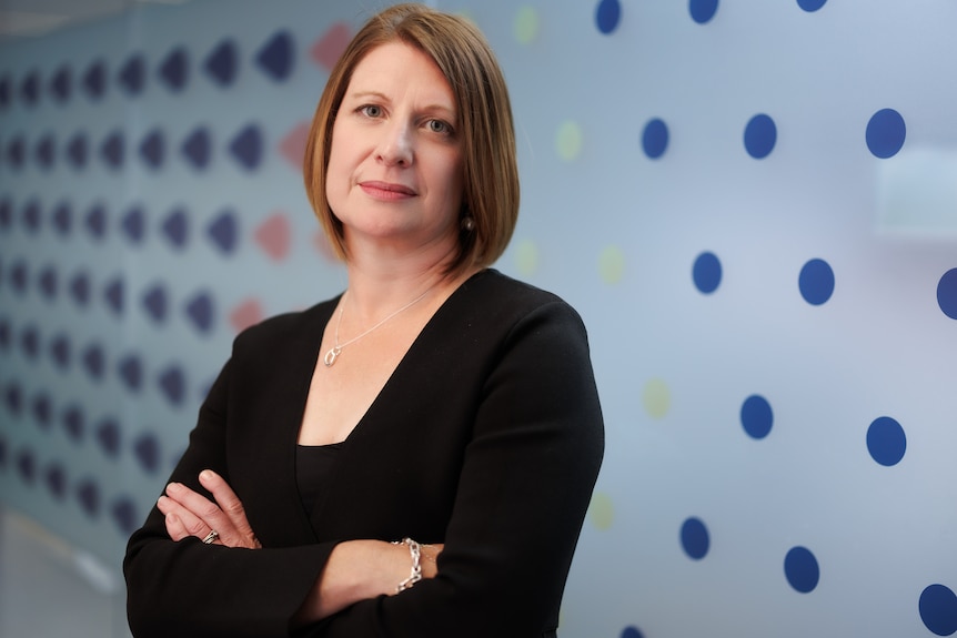 A woman is standing with her arms crossed looking into the camera