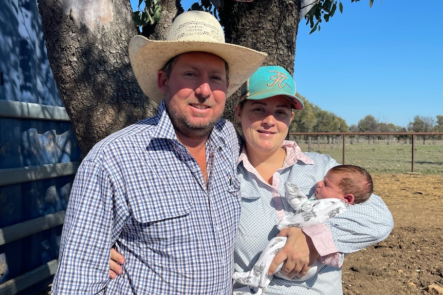 A man in a blue shirt and cowboy hat stands next to a woman holding a baby